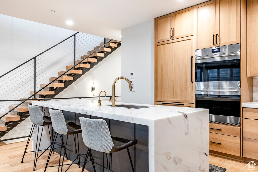 Kitchen featuring stainless steel double oven, light wood-style flooring, a breakfast bar area, light brown cabinetry, and recessed lighting