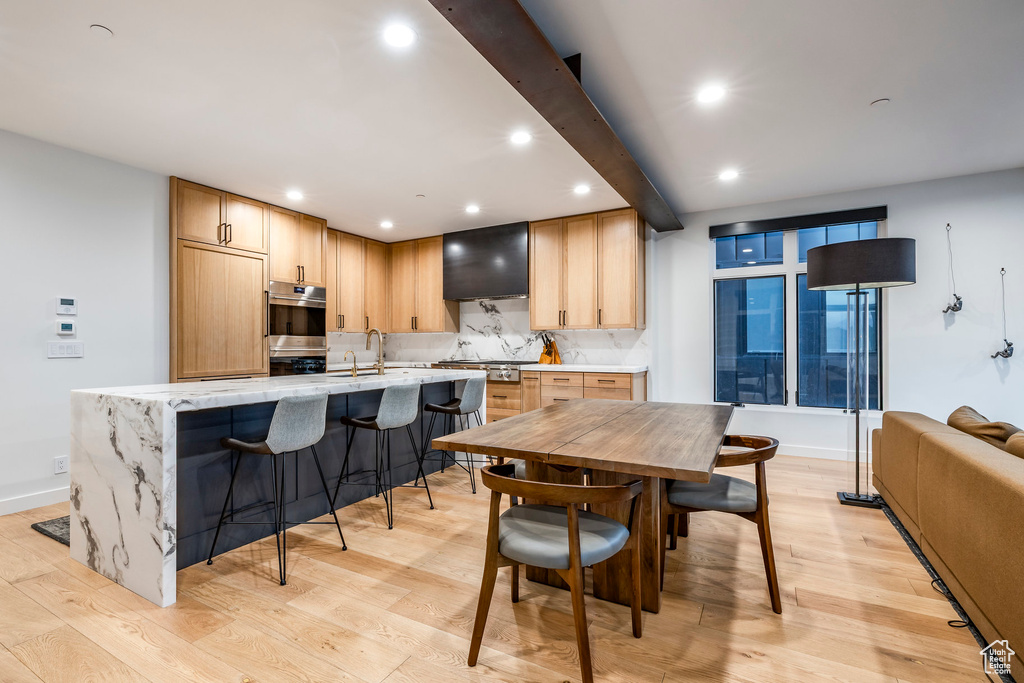 Kitchen featuring recessed lighting, light wood-style flooring, wall chimney exhaust hood, and decorative backsplash