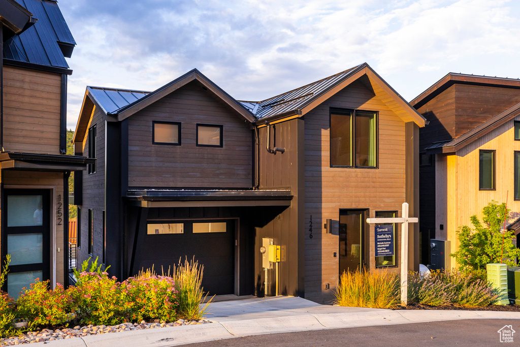 Modern home featuring a garage, concrete driveway, a metal roof, and a standing seam roof
