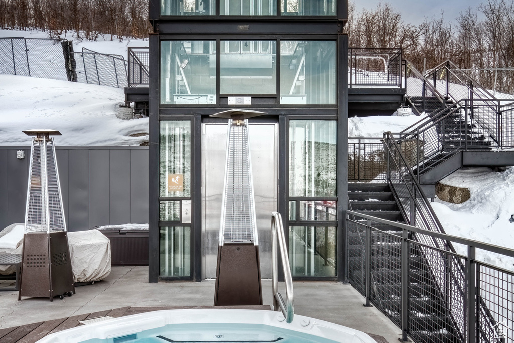 Snow covered back of property with stairs and an outdoor hot tub