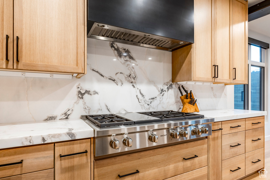 Kitchen with stainless steel gas cooktop, range hood, light brown cabinets, and backsplash