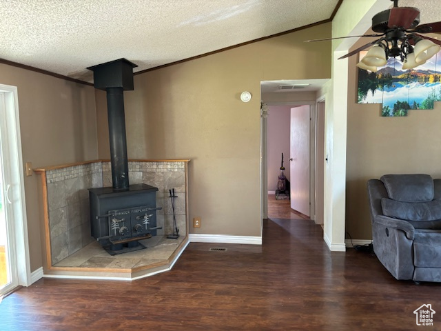 Unfurnished living room with wood finished floors, crown molding, a ceiling fan, a wood stove, and vaulted ceiling
