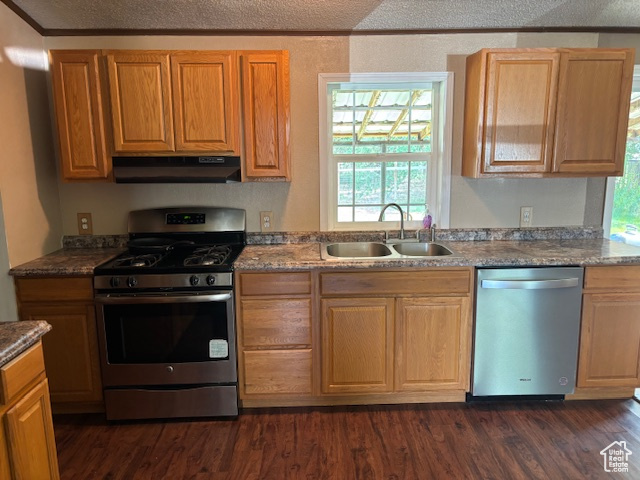 Kitchen featuring appliances with stainless steel finishes, under cabinet range hood, dark wood-type flooring, and crown molding