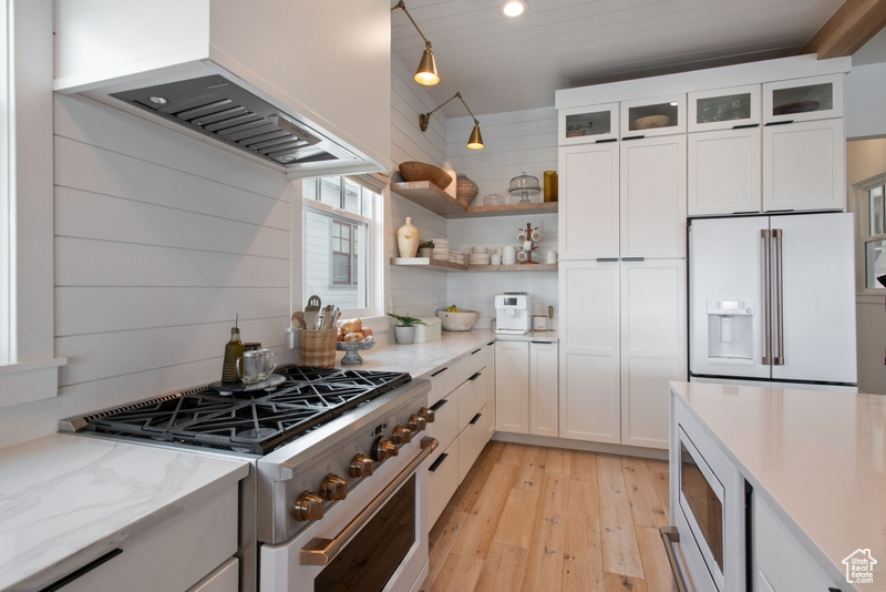 Kitchen with white appliances, custom exhaust hood, light wood-style flooring, white cabinetry, and glass insert cabinets