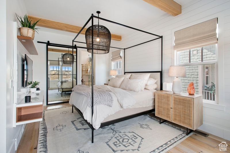 Bedroom with beamed ceiling, wood finished floors, and a barn door