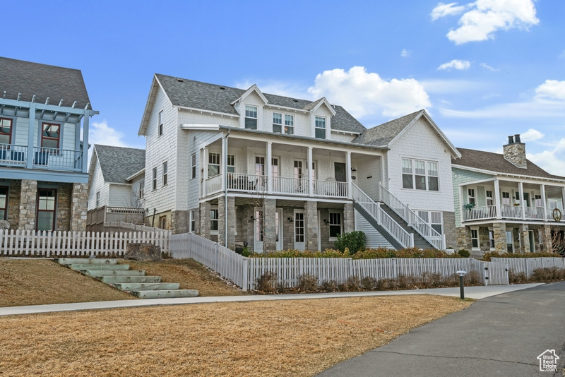 Multi unit property with a fenced front yard, covered porch, stone siding, roof with shingles, and a gate