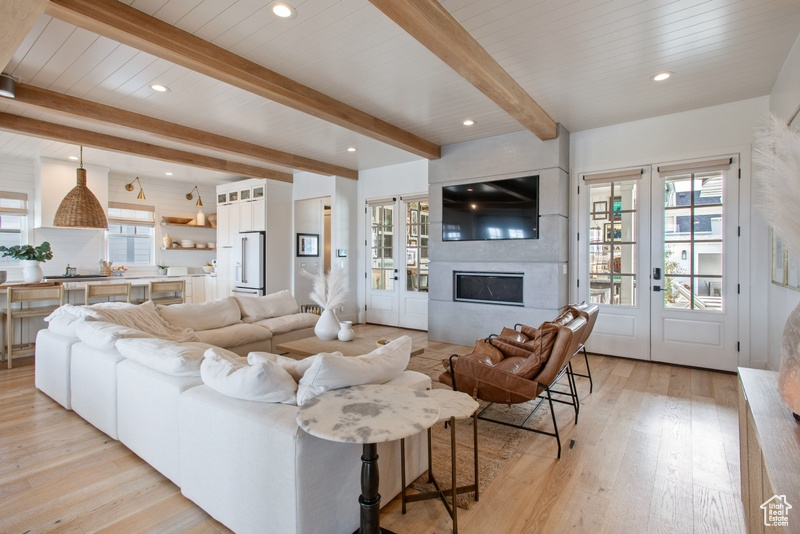 Living area with a fireplace, light wood finished floors, beam ceiling, recessed lighting, and french doors