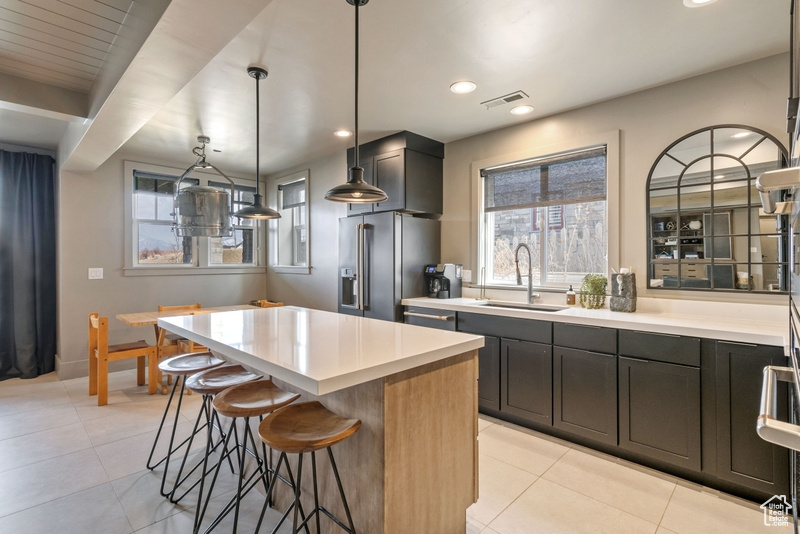 Kitchen with stainless steel appliances, a breakfast bar area, light tile patterned floors, a center island, and light countertops