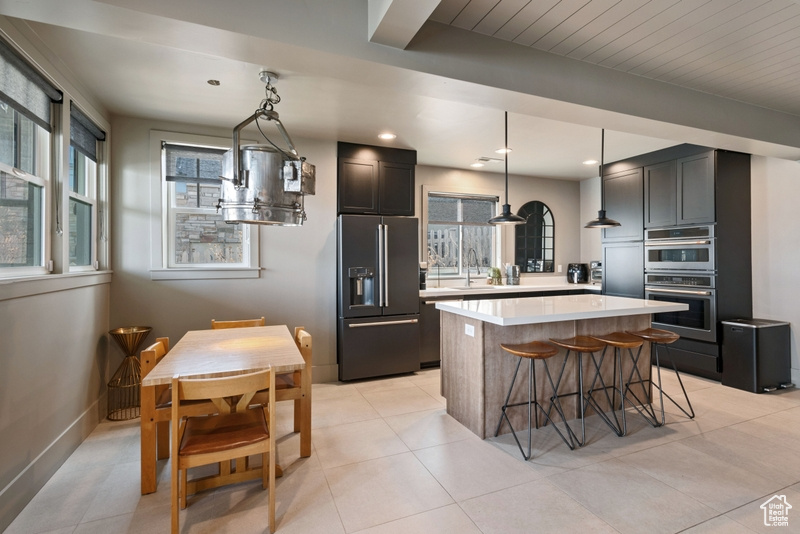 Kitchen featuring appliances with stainless steel finishes, light countertops, a center island, a breakfast bar, and pendant lighting
