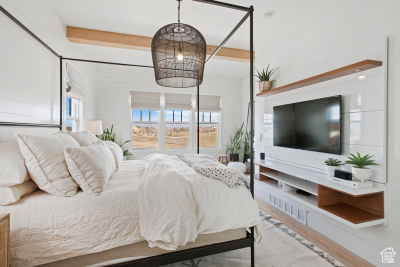 Bedroom with wood finished floors, multiple windows, and beamed ceiling
