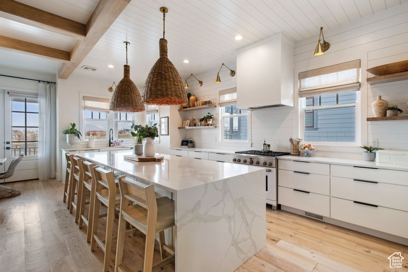 Kitchen with open shelves, high end stainless steel range, light wood-style floors, white cabinets, and a kitchen island