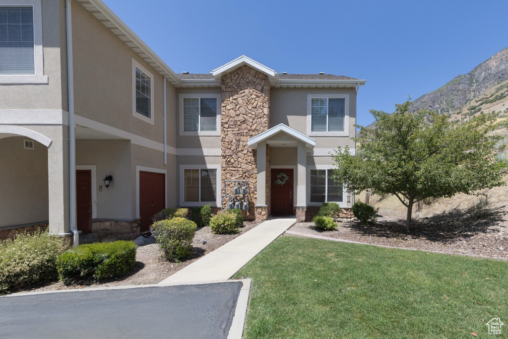 View of front of home with stone siding, stucco siding, a front yard, and a mountain view