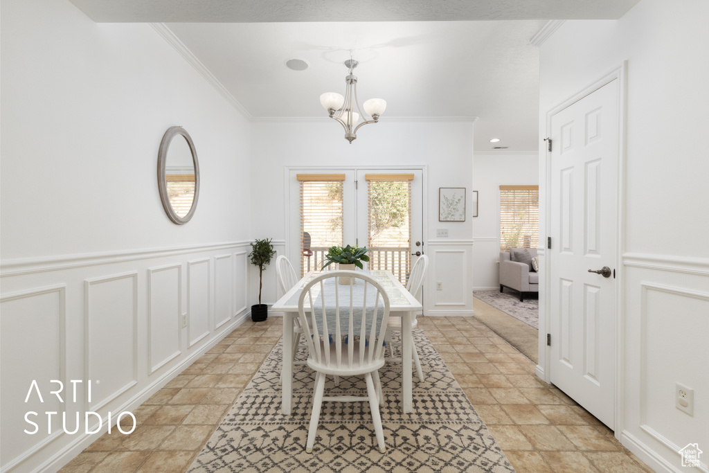 Dining area with crown molding, plenty of natural light, a decorative wall, a chandelier, and stone tile floors