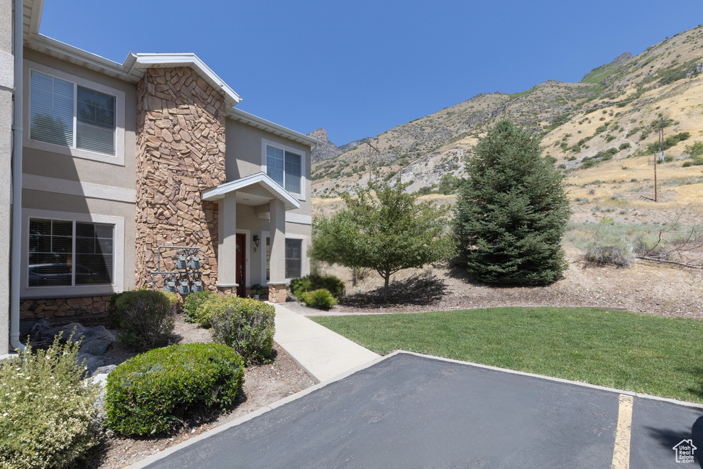 View of front of property featuring stone siding, stucco siding, a mountain view, and a front lawn