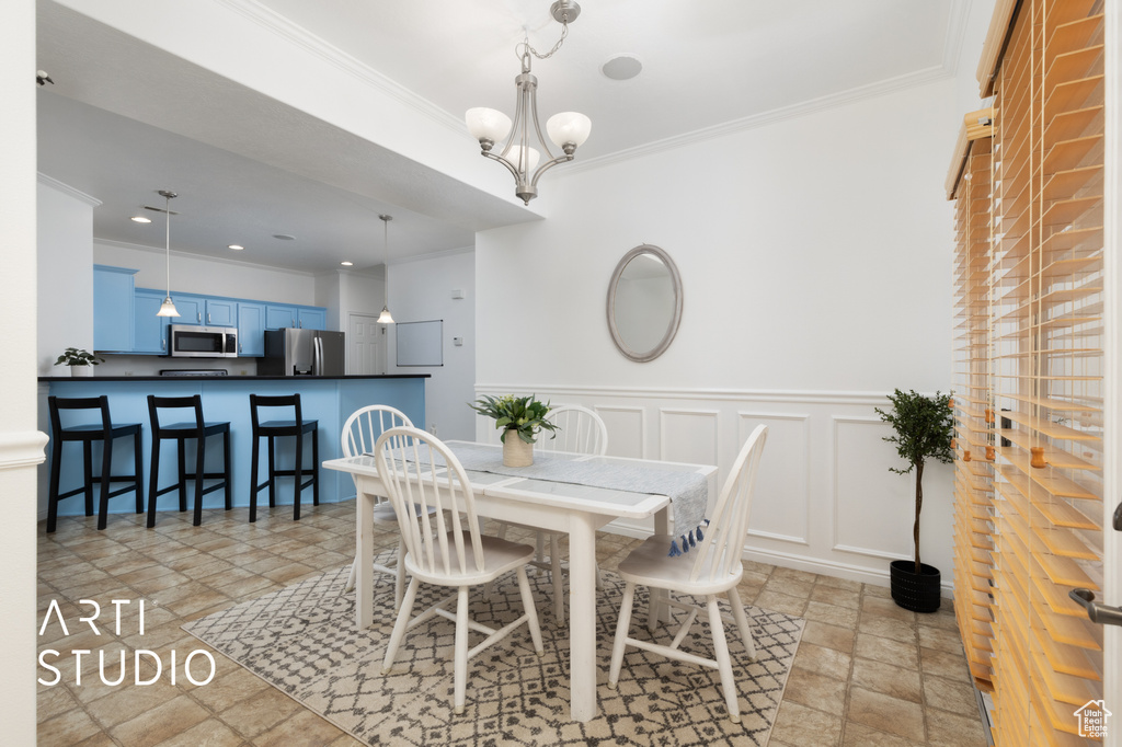 Dining area with crown molding, stone tile floors, a chandelier, a wainscoted wall, and a decorative wall
