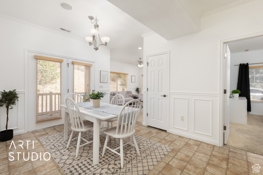 Dining area with ornamental molding, light stone finish floors, a chandelier, ceiling fan, and a decorative wall