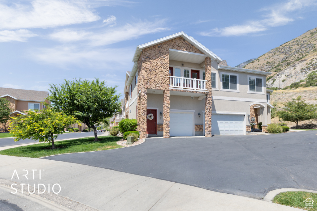 View of front of house featuring stone siding, stucco siding, a garage, a balcony, and driveway