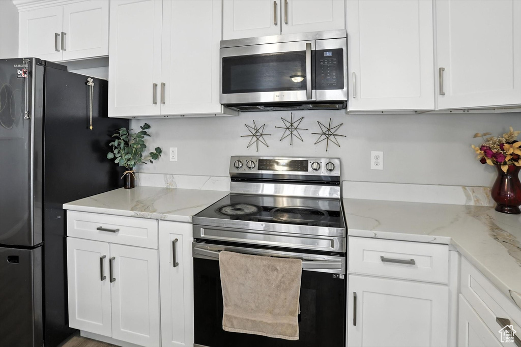 Kitchen with stainless steel appliances, white cabinets, and light stone countertops