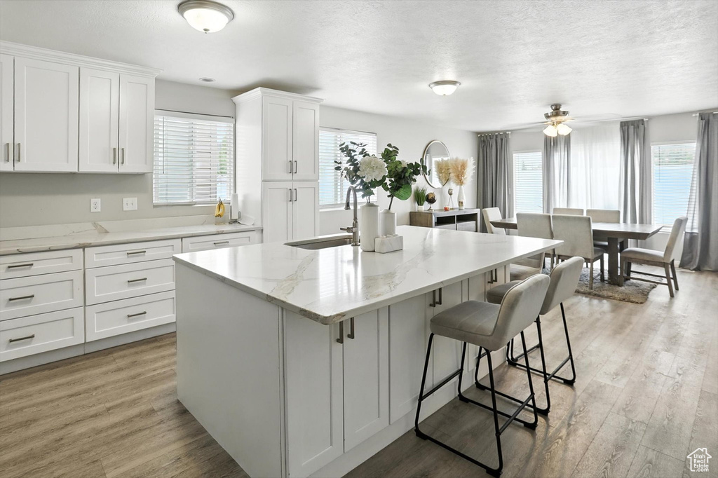Kitchen with a kitchen island with sink, a breakfast bar area, white cabinetry, a textured ceiling, and light wood-style flooring