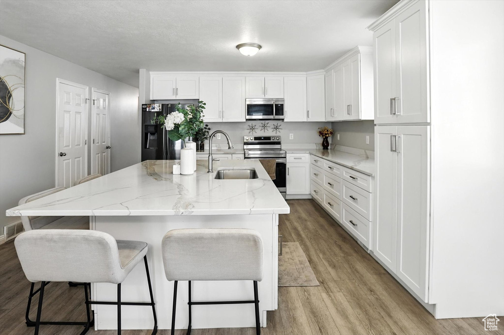 Kitchen featuring stainless steel appliances, light wood finished floors, white cabinets, a kitchen bar, and an island with sink