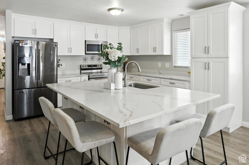 Kitchen featuring appliances with stainless steel finishes, white cabinetry, wood finished floors, and a kitchen bar