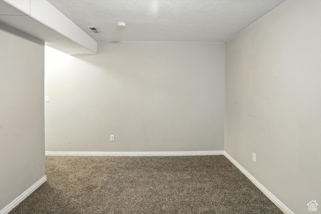 Empty room with carpet floors, a smoke detector, and a textured ceiling