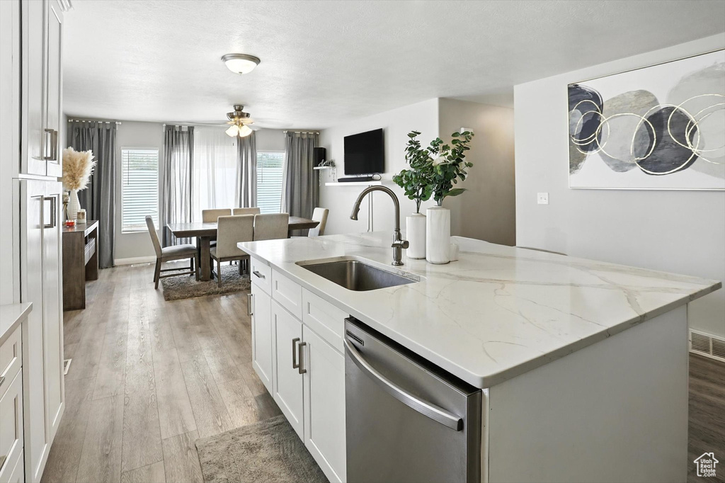 Kitchen featuring dishwasher, a center island with sink, light wood finished floors, and white cabinetry