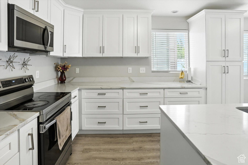 Kitchen with range with electric stovetop, stainless steel microwave, white cabinetry, light wood-style flooring, and light stone countertops