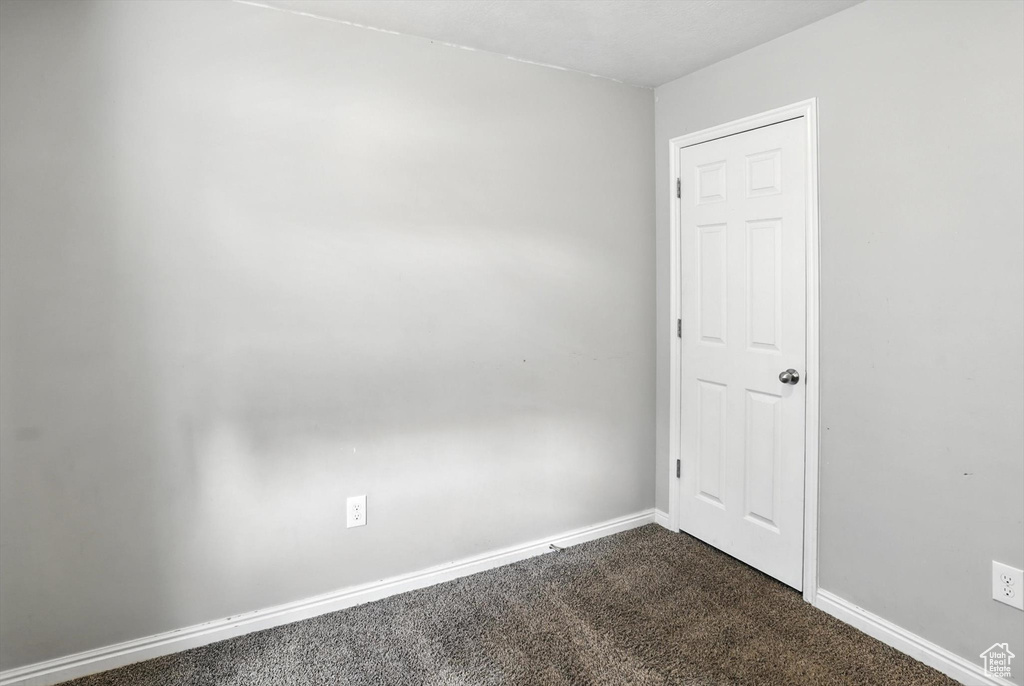 Empty room featuring dark carpet and baseboards