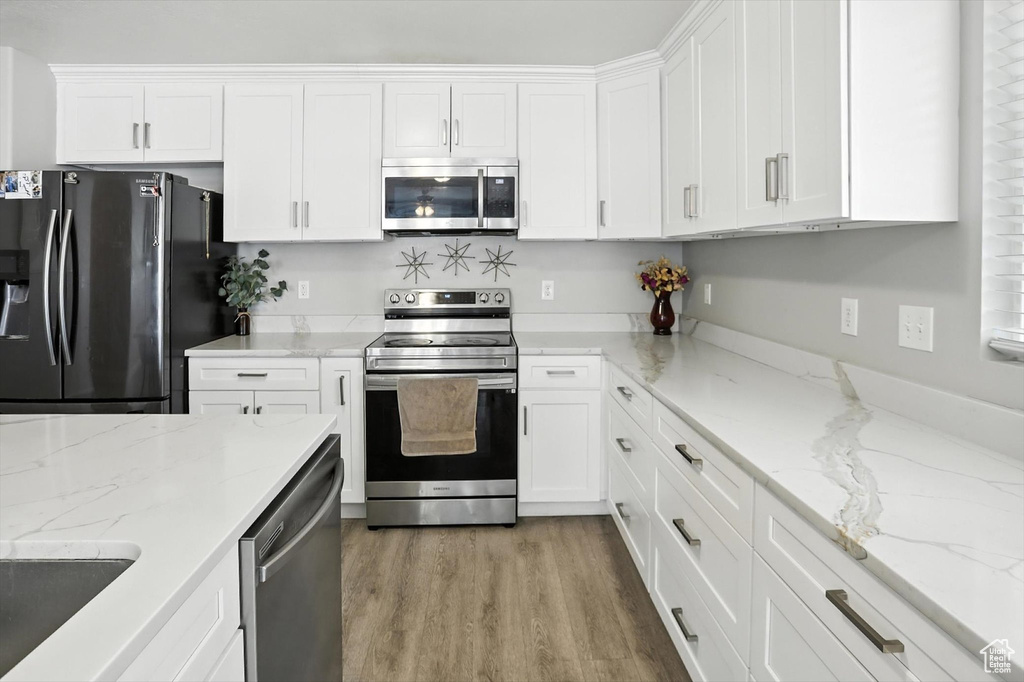 Kitchen featuring appliances with stainless steel finishes, white cabinets, light wood-type flooring, and light stone countertops