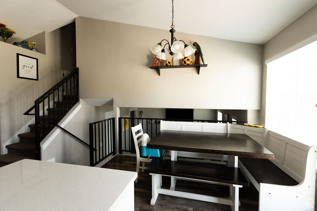 Dining space featuring a chandelier, dark wood-style floors, stairway, and vaulted ceiling
