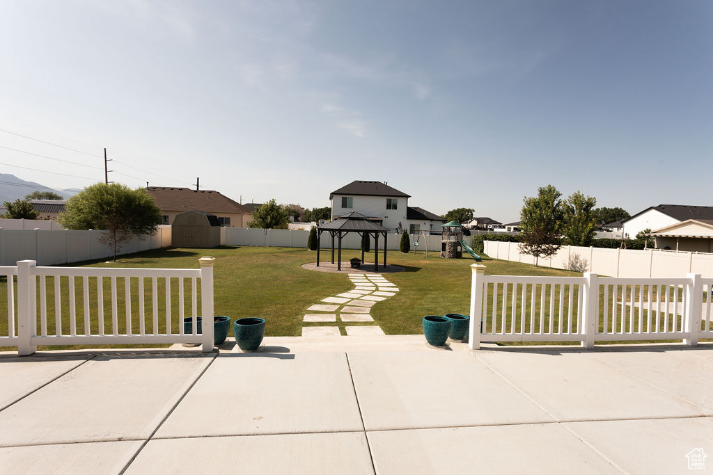 Fenced backyard featuring a patio area, a gazebo, a playground, a storage unit, and a residential view