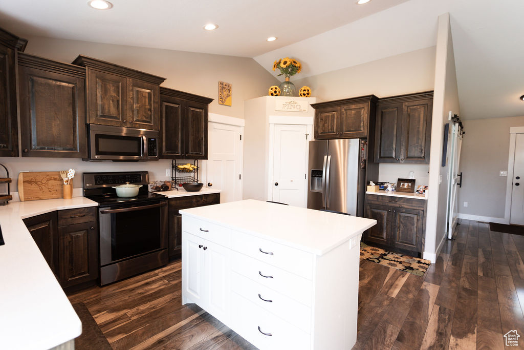 Kitchen with appliances with stainless steel finishes, lofted ceiling, light countertops, dark brown cabinets, and a kitchen island