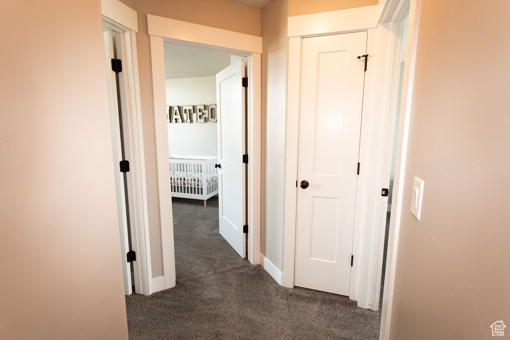 Hall featuring dark colored carpet and baseboards