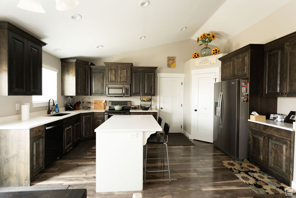 Kitchen with stainless steel appliances, light countertops, a center island, lofted ceiling, and a kitchen breakfast bar
