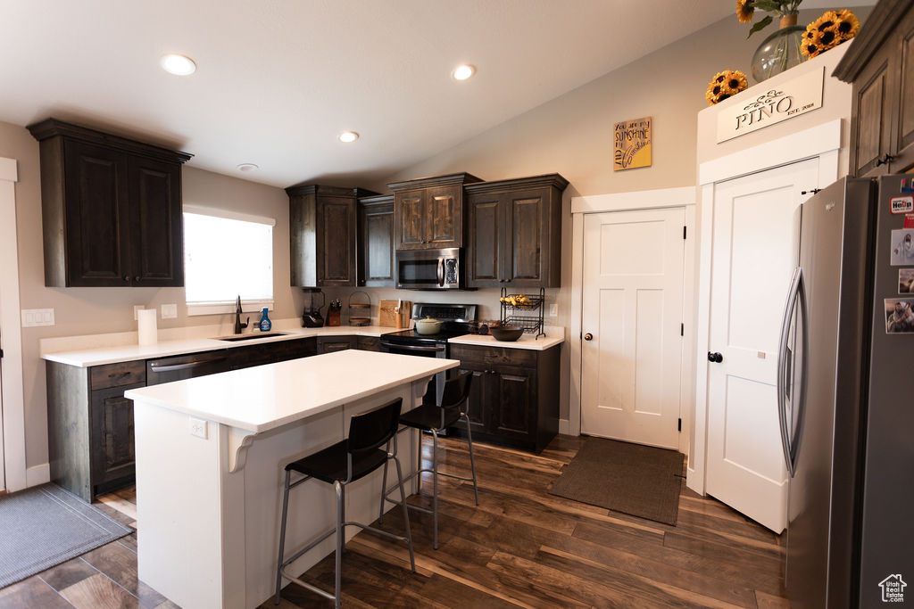 Kitchen featuring appliances with stainless steel finishes, a breakfast bar area, dark brown cabinets, light countertops, and lofted ceiling
