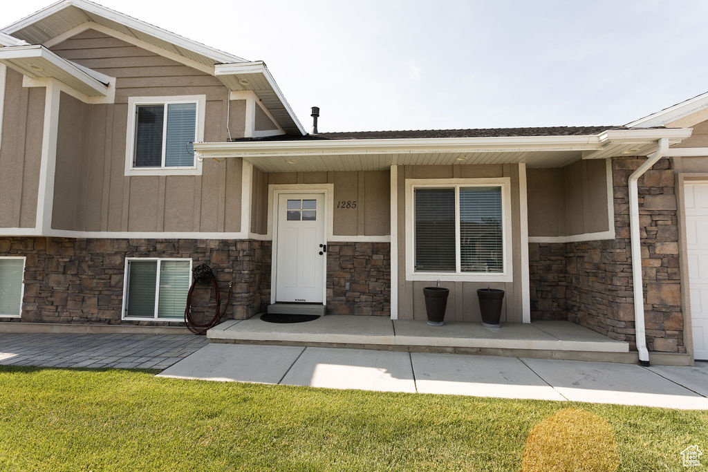 Property entrance with stone siding, covered porch, board and batten siding, and a lawn