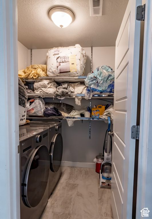 Washroom with washing machine and clothes dryer, a textured ceiling, and light marble finish flooring