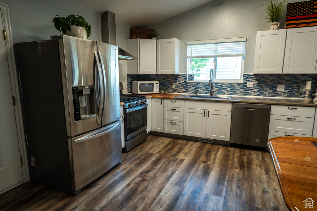 Kitchen with stainless steel appliances, vaulted ceiling, backsplash, dark wood-type flooring, and white cabinetry