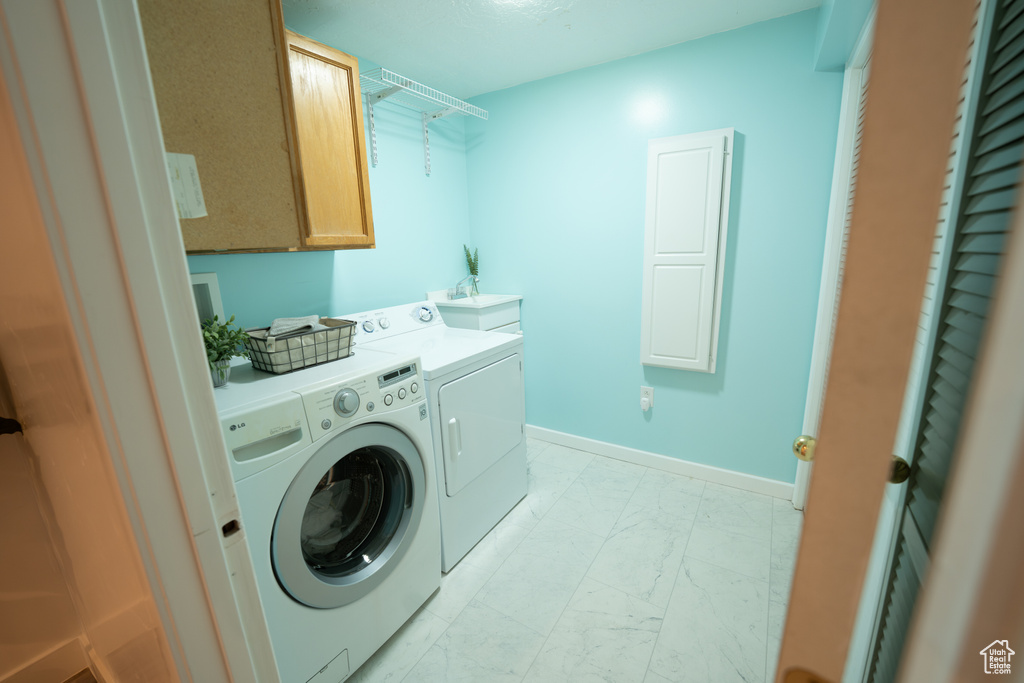 Washroom featuring independent washer and dryer, light marble finish floors, and cabinet space