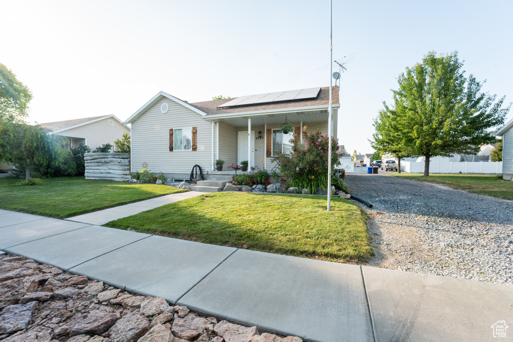 Ranch-style house with solar panels, covered porch, and a shingled roof