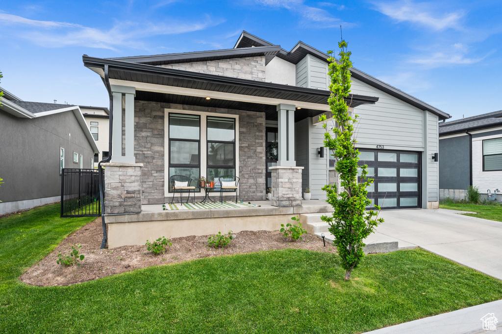 View of front of home with stone siding, a porch, driveway, and a front yard