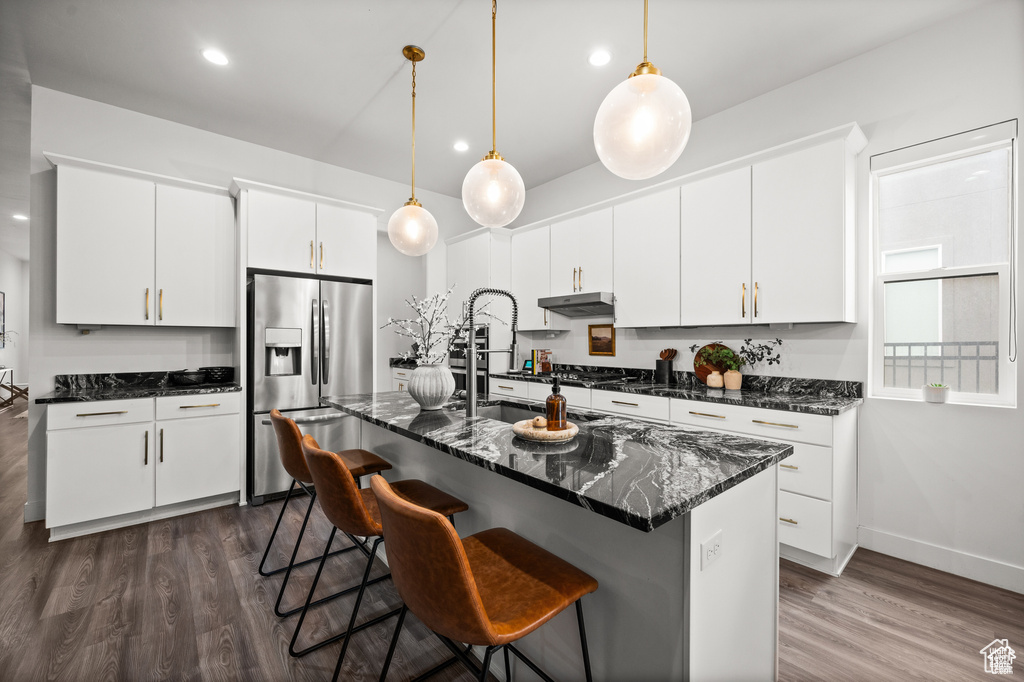 Kitchen with stainless steel fridge with ice dispenser, dark wood-style floors, pendant lighting, under cabinet range hood, and white cabinetry