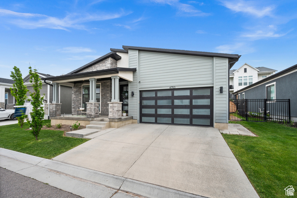 View of front of property featuring a porch, concrete driveway, stone siding, and a garage