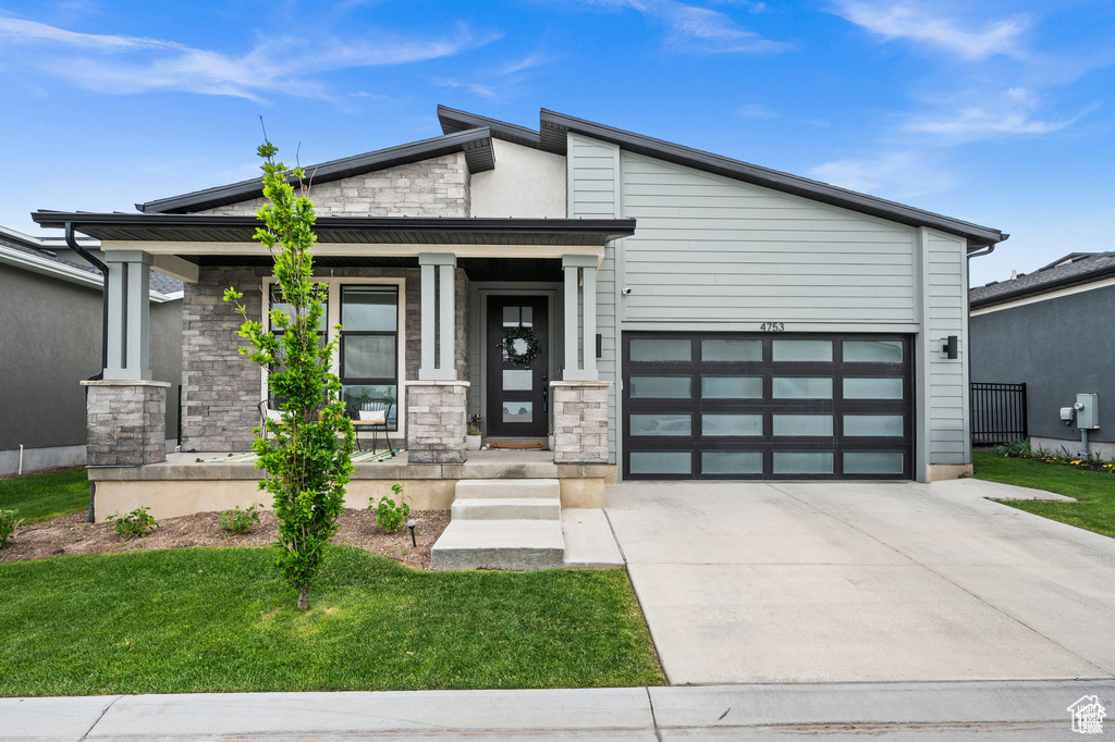 View of front of property with stone siding, driveway, a garage, a porch, and a front yard