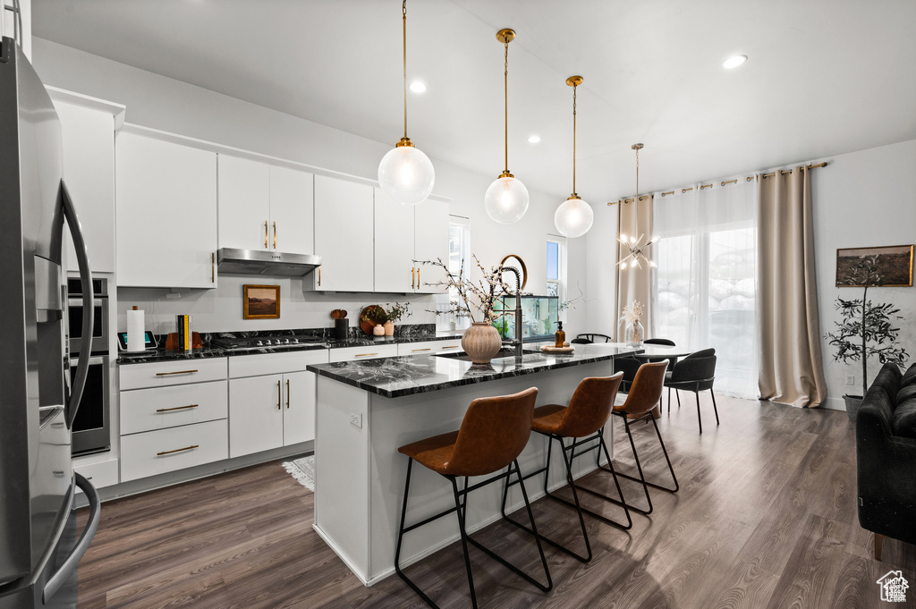 Kitchen featuring under cabinet range hood, a breakfast bar area, dark wood finished floors, a kitchen island, and white cabinetry