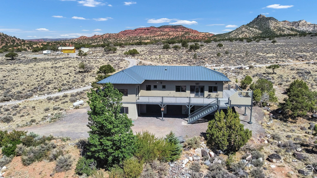 Rear view of house featuring stairs, view of desert, stucco siding, a metal roof, and a deck with mountain view