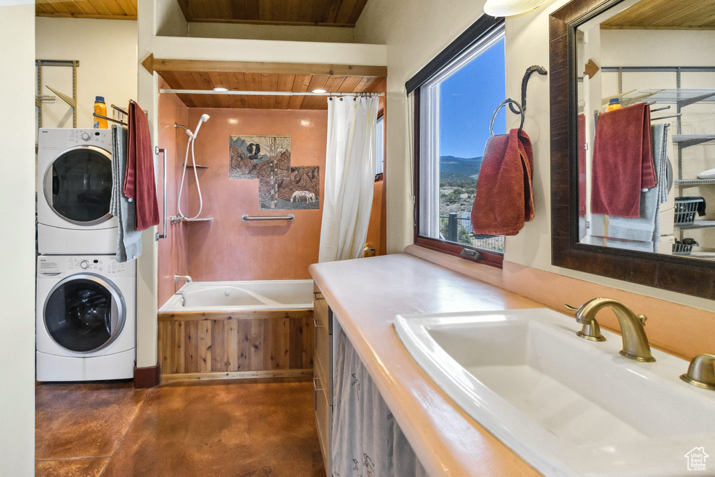 Bathroom with wooden ceiling, stacked washing machine and dryer, finished concrete flooring, vanity, and shower / bath combination with curtain