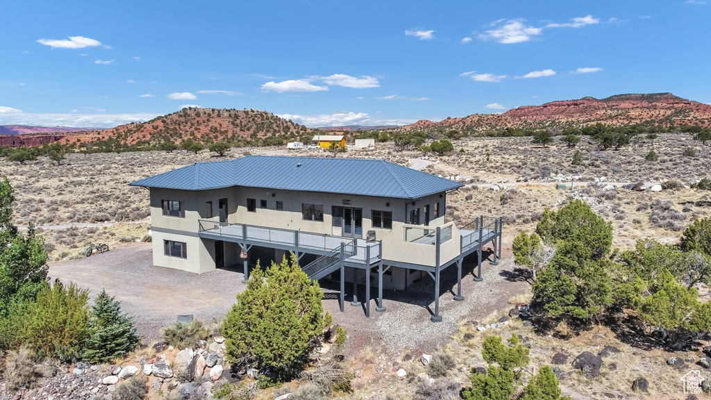 Rear view of house featuring a deck with mountain view, stucco siding, a metal roof, and view of desert landscape