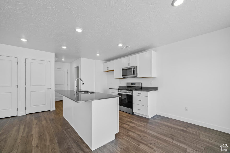 Kitchen featuring appliances with stainless steel finishes, dark countertops, white cabinets, dark wood-type flooring, and recessed lighting